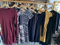 Lot of six women's dresses hanging on wooden hangers, showing variety in styles and colors including knit, patterned, and shirt dresses.