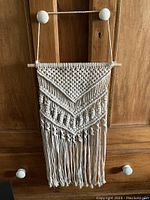 Front view of off-white macrame wall hanging with diamond and V-shaped knot pattern, wooden dowel at top for hanging.