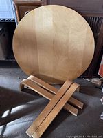 Round maple tabletop and four bentwood legs placed in front of furniture for display.