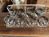 Top-front angled photo showing all 8 drinking glasses in their metal holder on a wooden surface.