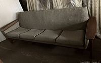 Front view of mid century modern sofa showing teak armrests and worn greenish-grey upholstery on cushions and backrest.