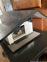 View of the custom birdhouse showing black angled roof, white walls, and textured base