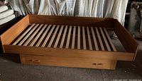 Full view of the teak platform bed showing wooden slat base and rolling drawer underneath.