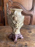 Front view of the beige stone Chinese vase showing 3D raised floral carvings and the wooden base.