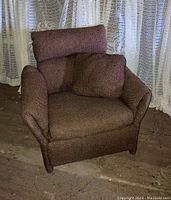 Front and angled view of the vintage brown upholstered armchair showing original fabric upholstery, loose side pillow, and attached headrest cushion on the backrest.