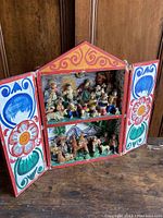 Full view of the colorful wooden retablo box with doors open showing the internal multi-figure scenes and floral painted doors.