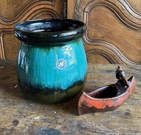 Photo showing Blue Mountain Pottery glazed pot with black rim and small brown-orange canoe figurine with visible chip