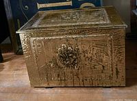 View showing front and side of the vintage box covered in detailed hammered brass with embossed figures and textured background.