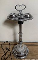 Full front view of floor ashtray showing chrome finish, ornate column, two lidded ashtray cups, heart-shaped handle and stone base with plug-in cord.