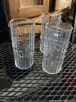 Three vintage clear glass Iittala Tapio glasses with vertical ridges and raised bubbles arranged on metal mesh surface.
