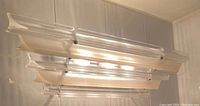 Vintage Lucite light fixture mounted on ceiling, illuminated, showing clear horizontal acrylic rods and stepped design.