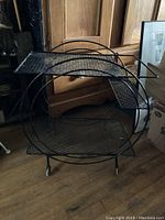Full view of vintage black metal bar cart showing circular side frames and three mesh shelves.