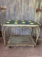 Full front view of vintage mid century bar cart showing tiled top and metal frame with wheels.
