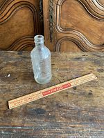 Clear vintage Pepsi glass bottle and wooden Coca Cola ruler on wooden surface and background.
