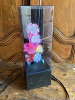 Full view of the fiber optic light with black base and plastic casing, showing colorful fabric flowers inside.