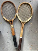 Pair of vintage wooden tennis racquets side-by-side on floor, showing overall view and condition.