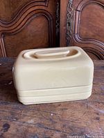 Vintage yellow rectangular ceramic butter dish with lid on wooden surface, showing front and side profile.