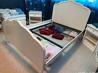 Full view of white wooden bed frame including headboard, footboard, and metal side rails in a room setting with other furniture.