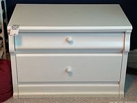 Front view of the white wood two-drawer dresser with round white knobs, showing the smooth painted finish and no visible damage.