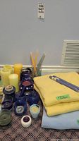 Photo showing two yellow and one blue folded fleece throw blankets with several candles in various colors and holders, including taper candles, pillar candles, tealights, and votives.