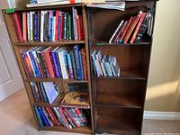 Two wooden bookcases side by side, one wider and filled with books, the other narrower with gothic cutouts on the side and fewer items.