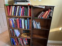 Two wooden bookshelves filled with assorted books including fiction, wellness, religious topics, and a few CDs and magazines on the shelves.