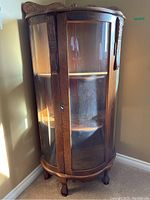 Full view of the wooden cabinet with curved glass front, showing the carved wood details and curved glass door.