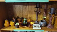 Shelf with two metal candle holders, star-shaped glass dish, and decorative glass fruit in amber and green colors.
