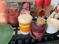 View of assorted candles and decorative items on a black grid surface including pink and red candles, Pier 1 Imports candle, angel decorations, and figurines