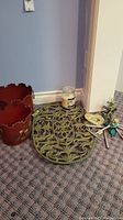 Photo showing decorative oval metal grate, small candle, frog figurine, and wind chimes on carpeted floor.