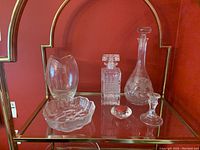 Glassware items displayed on glass shelf with red wall background, including decanters and candle holders.