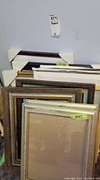 Stacked assorted photo frames in various finishes and sizes, with size labels visible for some frames (25x18 and 14x7).
