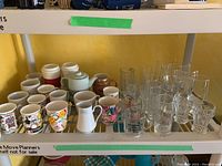 Shelf with an assortment of coffee mugs, glassware, and a white ceramic teapot.