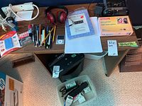 Photo showing the unboxed office supplies including the iPod, headphones, pens, hole punch, lamp, photo paper, and clock radio on a desk, with staples and miscellaneous small items in front.