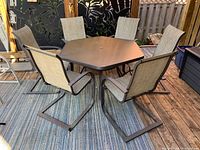 Hexagonal patio table with six matching mesh chairs arranged around it on a wooden deck.