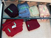 Photo showing multiple sets of queen-size linens including sheets, pillowcases, and duvet covers in different colors arranged on a shelf.