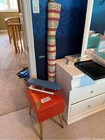 Photo showing vintage orange sewing stool with blue ironing board accessory and decorative fabric roll in background.