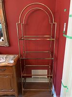Full front view of the metal frame shelving unit showing the arch design and all four glass shelves against a red wall.