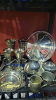 Photo showing silverplate goblets, creamer, sugar bowl, trays, and utensil holders on black shelf