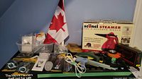 Photo showing overall contents including steamer box, glue guns, tools, Canadian flag and assorted hardware items