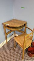 Vintage wooden telephone table with hinged wooden chair tucked under it, displayed in room corner on carpet.