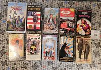 Front view of the 10 VHS movies lying on a surface, showing colorful cover art including The Quest for Camelot, Patton, The Wizard of Oz, Death to Smoochy, and others.