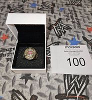 Close-up photo of 1930 Montreal Canadiens Stanley Cup replica ring in a white Pandora box on a metal patterned surface.