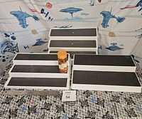 Front view of the two white tiered display stands showing black anti-slip mats on each tier, with one orange spice container for scale.