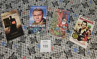 Front view of 4 sealed VHS tapes laid out on a patterned fabric surface, showing cover art and titles: Gladiator, The Great Escape, The First Christmas, Dillinger.