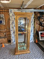 Full view of the wood and glass display cabinet showing front and glass shelves with the light on.