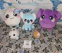Five SQUEEZAMALS plush toys displayed on patterned fabric, including unicorn, koala, elephant, and two smaller plush toys.