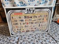 Framed complete Kenner Star Wars action figure guide poster with figures from 1978 to 1985, displayed on carpeted floor.