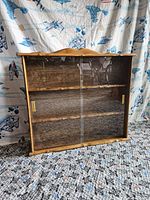 Front view of the wooden wall cabinet showing glass sliding doors and brass handles.