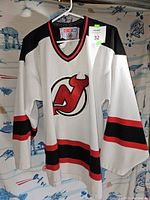 Front view of white CCM hockey jersey with New Jersey Devils logo, red and black striping
